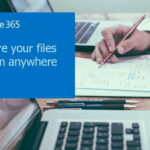 A man writing on a paper beside two laptops